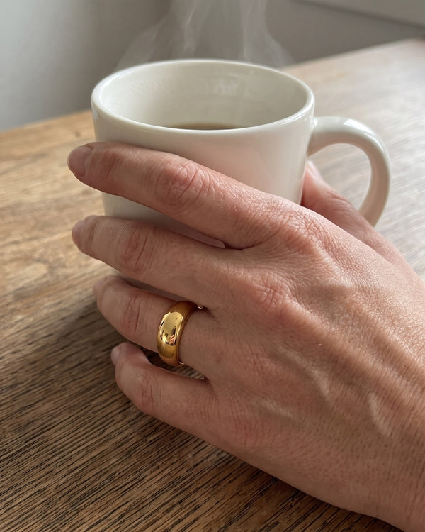 Gold dome ring on a hand holding a mug